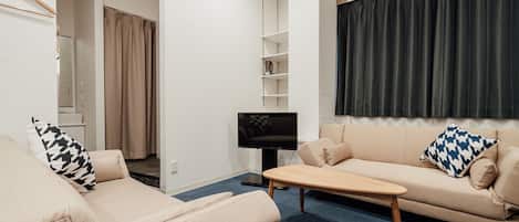 Ein modernes Wohnzimmer mit einem beigefarbenen Sofa, einem Holztisch und einem Fernseher auf einem Schrank.
