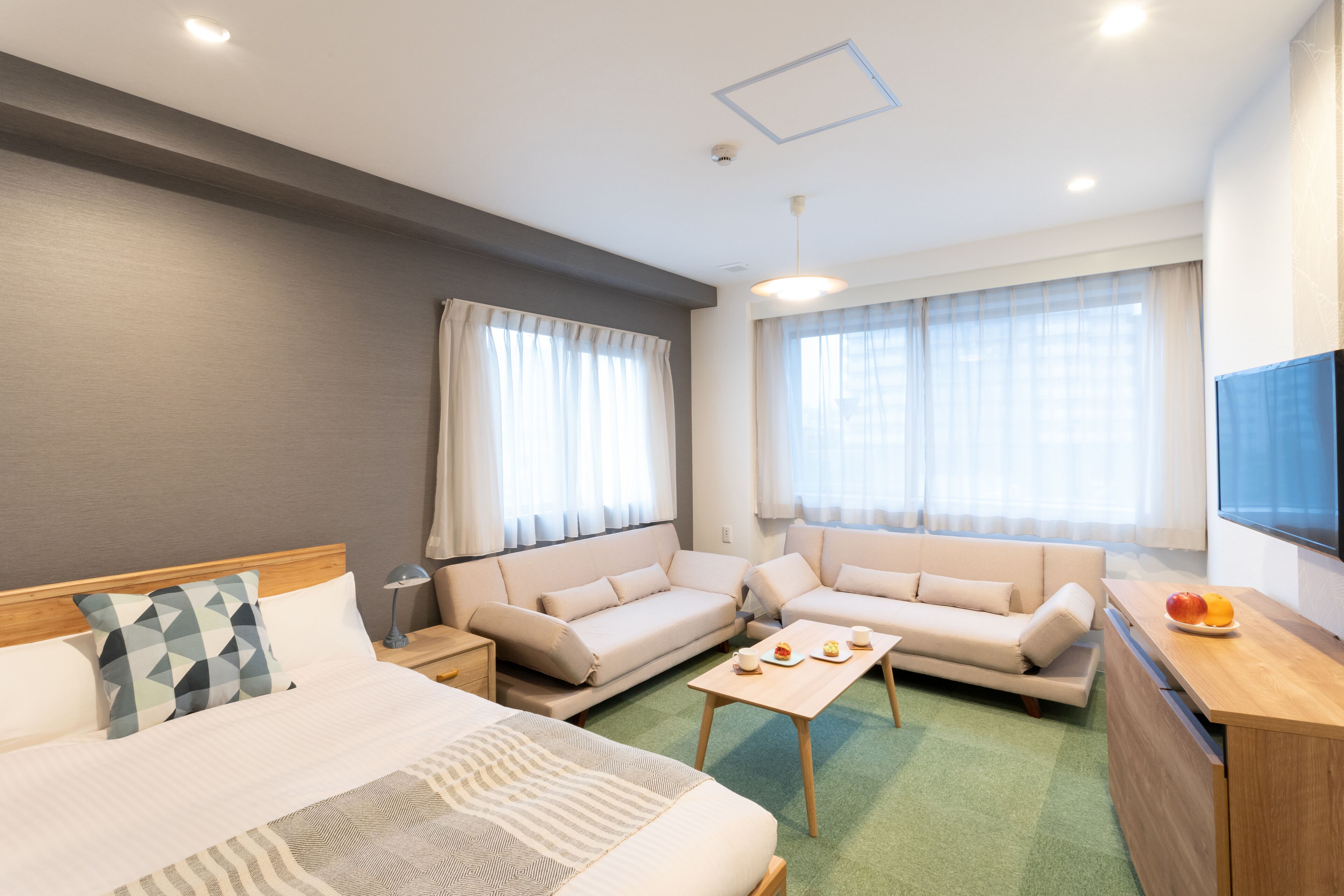 A hotel room with a bed, two sofas, a small table, and a TV.