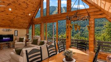 A wooden interior with a TV, sofas, and a dining table with chairs.