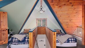 Un dormitorio tipo ático triangular con dos camas, un ventilador de techo y una ventana.