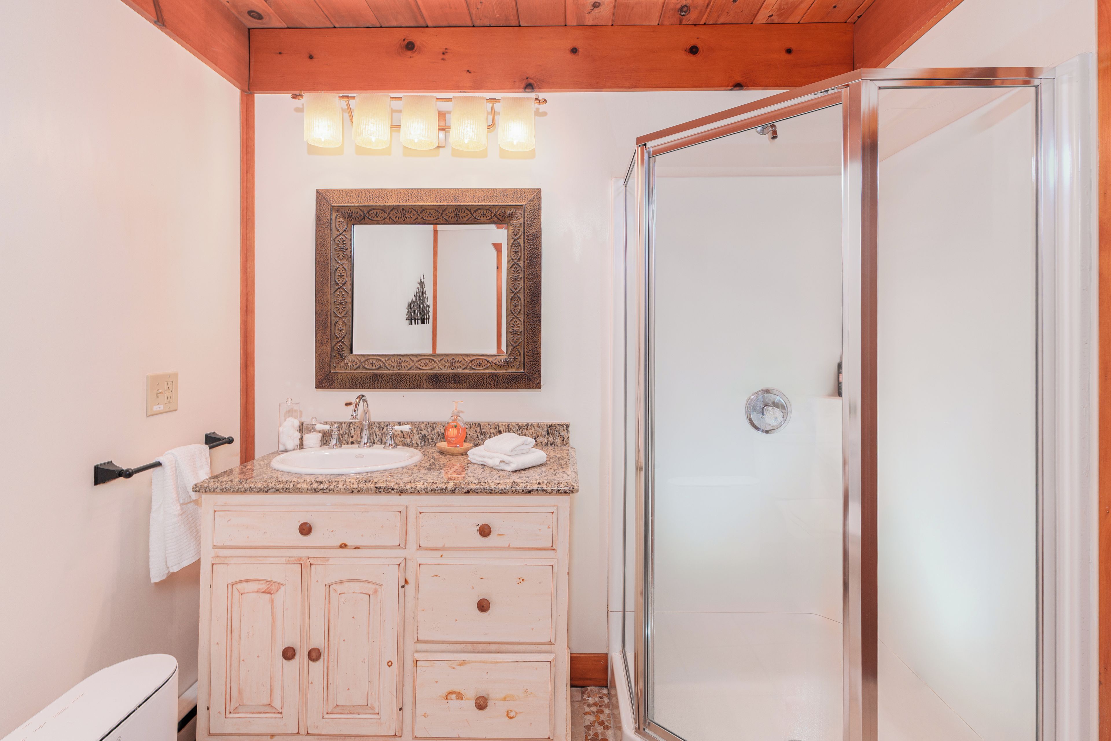 Un baño con techo de madera, un lavabo con espejo y una zona de ducha.