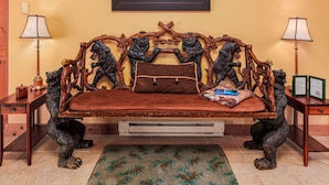 Un sofá con cojín de cuero marrón, flanqueado por dos reposabrazos de madera con esculturas de animales, un cuadro en la pared y dos lámparas a cada lado.