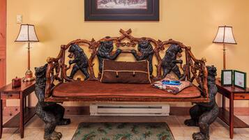 Un canapé doté d’un coussin en cuir marron, flanqué de deux accoudoirs en bois ornés de sculptures d’animaux, un tableau encadré au mur et deux lampes de chaque côté.