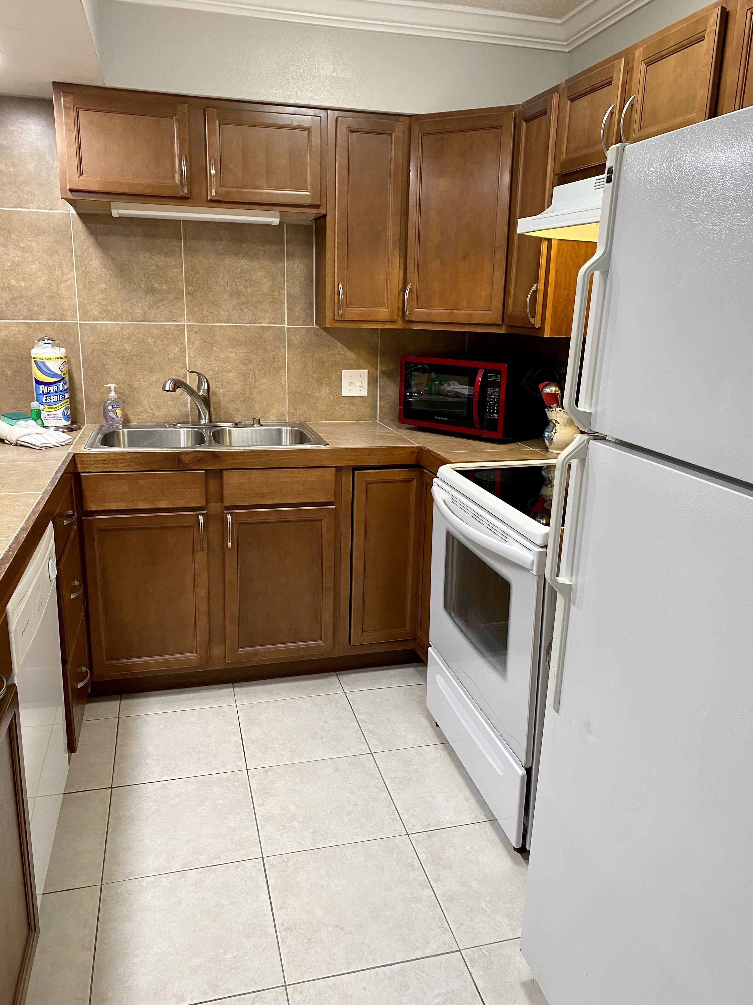 Una cocina con armarios de madera, un lavamanos de acero inoxidable, un microondas y un refrigerador blanco.