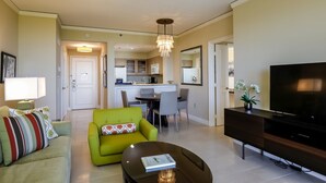 Un soggiorno moderno con un divano, una poltrona verde, un tavolino da caffè, una televisione a schermo piatto e una cucina sullo sfondo.