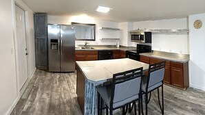 A modern kitchen with a stainless steel refrigerator, a microwave, a dishwasher, and a large island with bar stools.