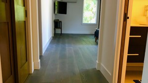 Un pasillo con suelo de madera que conduce a una habitación con ventana y televisor de pantalla plana montado en la pared.