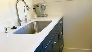 Una cocina con un lavamanos de acero inoxidable, una cafetera y armarios azul oscuro.