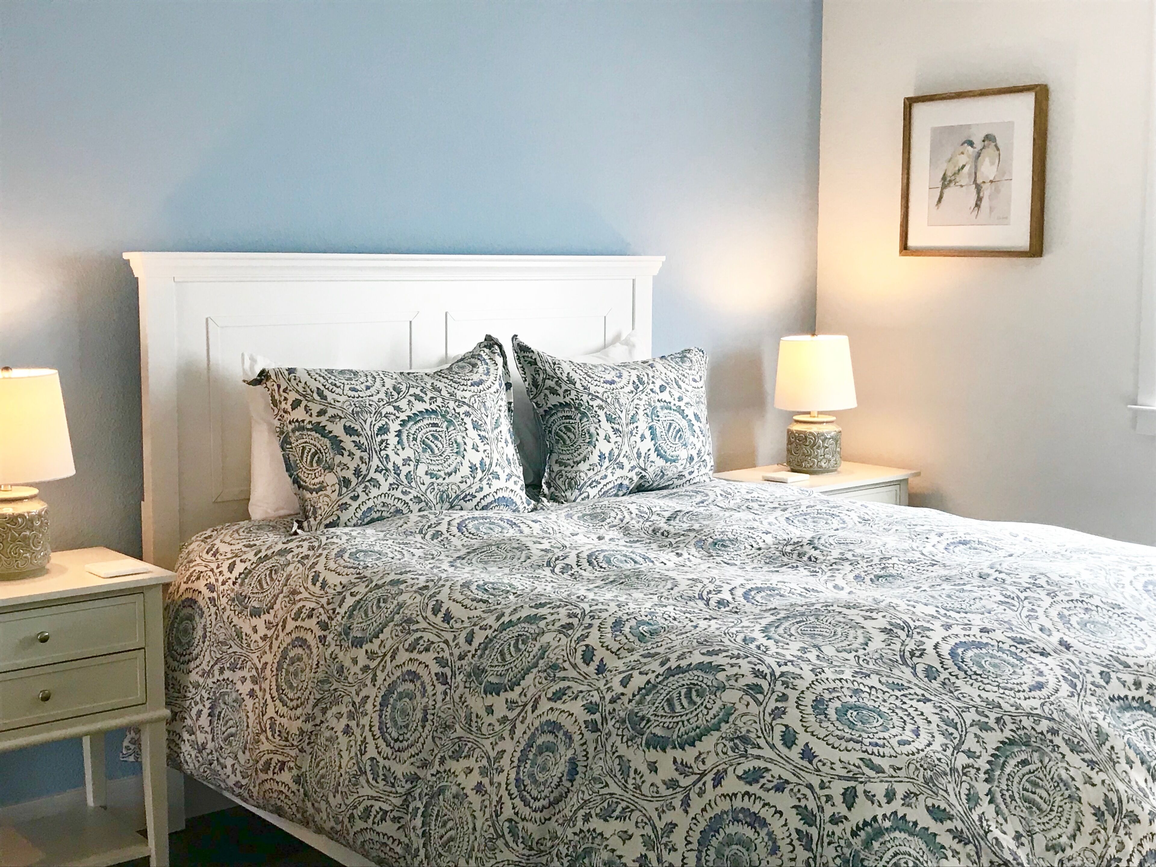 Een slaapkamer met een bed, twee nachtkastjes, een lade en een ingelijste foto aan de muur.