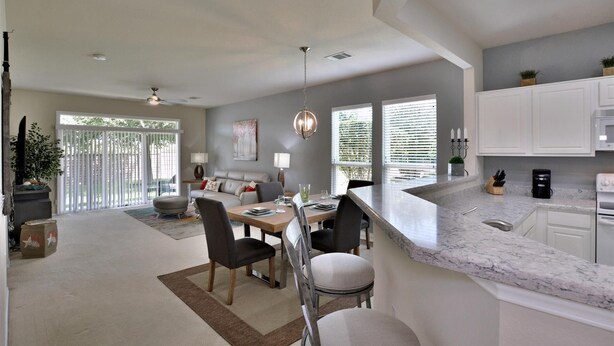 A modern kitchen with white cabinets, a marble countertop, and a dining area with a table and chairs. - SUN CITY GEORGETOWN, TX RESORT - STUNNING CONTEMPORARY! (Georgetown)