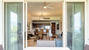 A spacious living area with a dining table and chairs, a ceiling fan, and a view through a sliding glass door to a kitchen and dining area. - E303-Beautiful front ocean condo (La Paz)