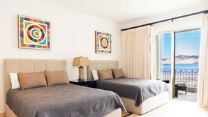 A hotel room with two beds, a nightstand, a lamp, and a view of the sea through a balcony. - E303-Beautiful front ocean condo (La Paz)