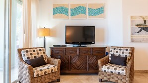 A living room with two wicker armchairs, a flat-screen TV, a wooden cabinet, and artwork on the walls. - E303-Beautiful front ocean condo (La Paz)