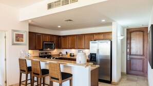 A kitchen with wooden cabinets, a central island with bar stools, a microwave, stove, refrigerator, and a coffee maker. - E303-Beautiful front ocean condo (La Paz)