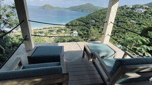Eine Terrasse mit Holzmöbeln und Blick auf das Meer und die Hügel.