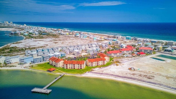 Vista aérea de um resort costeiro com vários edifícios, um cais e uma praia.