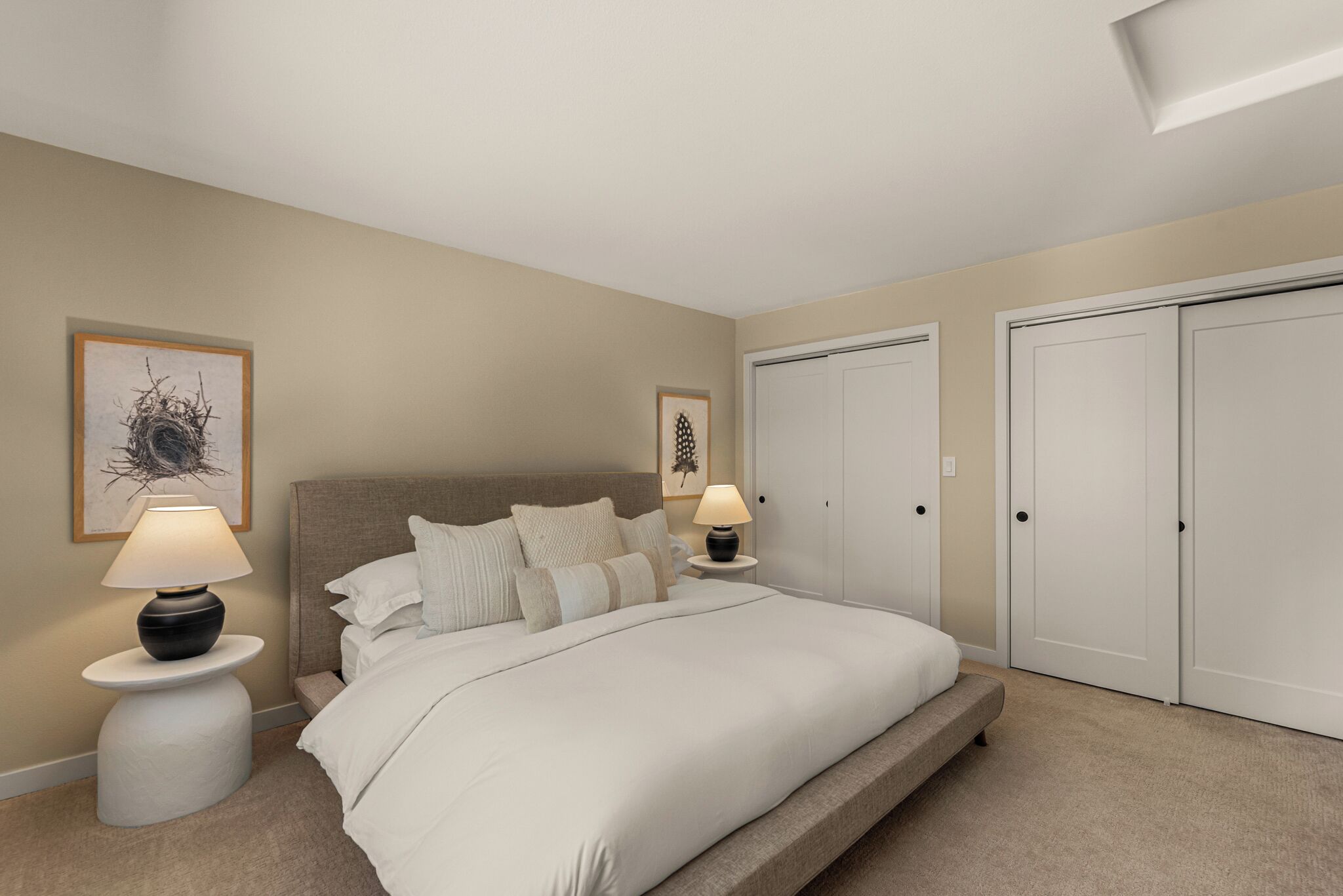 A bedroom with a bed, two bedside lamps, a nightstand, a framed artwork on the wall, and a closet with two doors.
