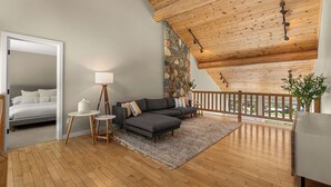 Ein modernes Interieur mit Holzboden, einer Steinwand, einem grauen Sofa, einem kleinen runden Tisch und einem Bett im angrenzenden Zimmer.