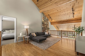 A modern interior with a wooden ceiling, a stone wall, a grey sofa, a small round table, and a bed in the adjacent room. - Fox Lodge: an oasis with amazing views (Leavenworth)