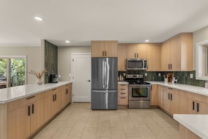 A modern kitchen with stainless steel appliances, wooden cabinets, and a large window. - Fox Lodge: an oasis with amazing views (Leavenworth)