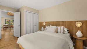 Ein Schlafzimmer mit einem Bett, Nachttischen, einem Holz-Kopfteil und einer Tür zu einem Essbereich.
