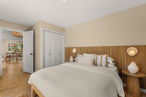 A bedroom with a bed, bedside tables, a wooden headboard, and a door leading to a dining area. - Fox Lodge: an oasis with amazing views (Leavenworth)