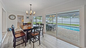 Un comedor con mesa y sillas de madera, una lámpara de araña y vistas a un patio trasero con piscina.