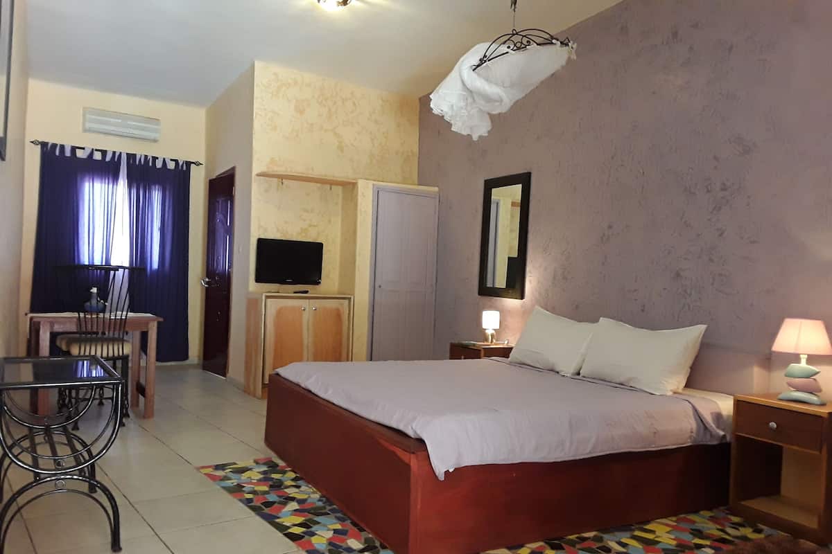 A hotel room with a bed, a desk, a chair, a television, a wardrobe, and a mirror.