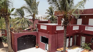A multi-story building with a red facade, a reception area, and a tiled courtyard with palm trees and a pool. - Grazia Maria Hotel (Mbour)