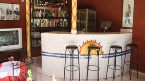 A bar area with a tiled counter, four stools, and a shelf with bottles. - Grazia Maria Hotel (Mbour)