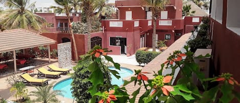 Zona junto a la piscina con sillones de descanso, un edificio de recepción y palmeras.