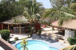 Un espace piscine avec des chaises longues, un bar et des palmiers.