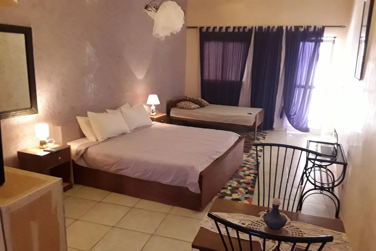 A hotel room with a large bed, a smaller bed, a desk with a chair, and a window with curtains.