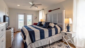 Ein Schlafzimmer mit einem Bett, einem Deckenventilator, einem Nachttisch mit Lampe, einem Schminktisch und einem Fenster mit Jalousien.