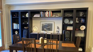 A dining area with a wooden table and chairs, surrounded by bookshelves filled with books and decorative items.