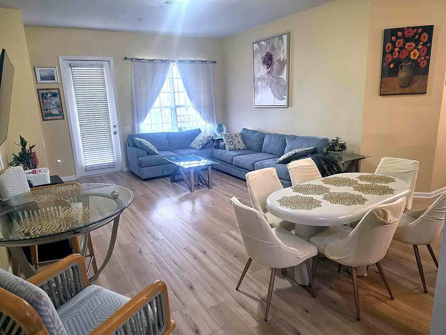 A living room with a sofa, coffee table, dining table with chairs, and a window with curtains.