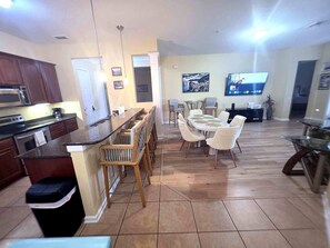 A spacious kitchen with a central island, dining area with chairs, a television, and a large window.