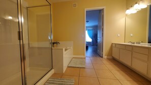 Un baño moderno con cabina de ducha de vidrio, bañera, espejo grande y tocador con lavabo doble.