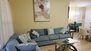 A living room with a grey sectional sofa, a glass coffee table, and a painting on the wall.