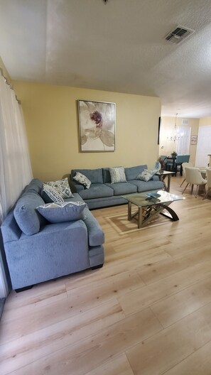 Una sala de estar con un sofá modular gris, una mesa de centro de vidrio y un cuadro en la pared.