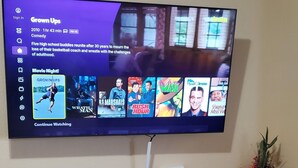 A flat-screen TV mounted on a wall above a black entertainment center with a printer and a vase with flowers.