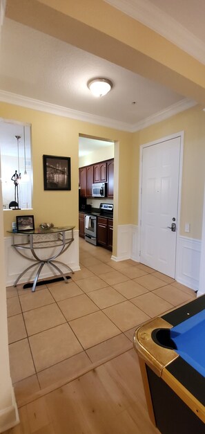 Una habitación con mesa de billar, zona de comedor con mesa de vidrio, cocina con armarios de madera y una puerta blanca.