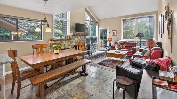 Un vaste espace de vie doté d’une cheminée, d’une table à manger avec des bancs, et d’un coin salon confortable avec un canapé et des fauteuils.