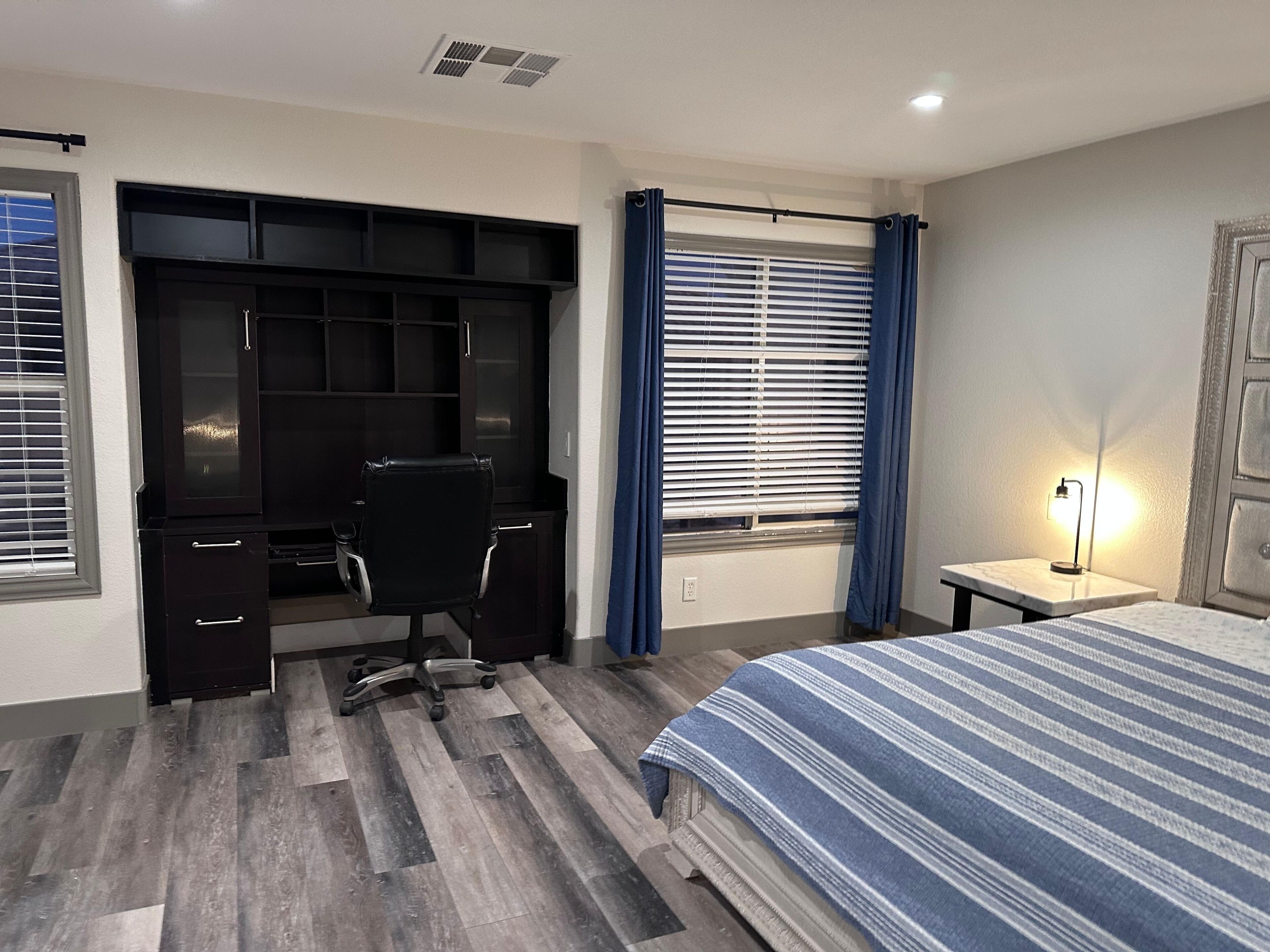 Ein Schlafzimmer mit einem Bett, einem Schreibtisch mit Stuhl, einem Kleiderschrank und einem Fenster mit Vorhängen.