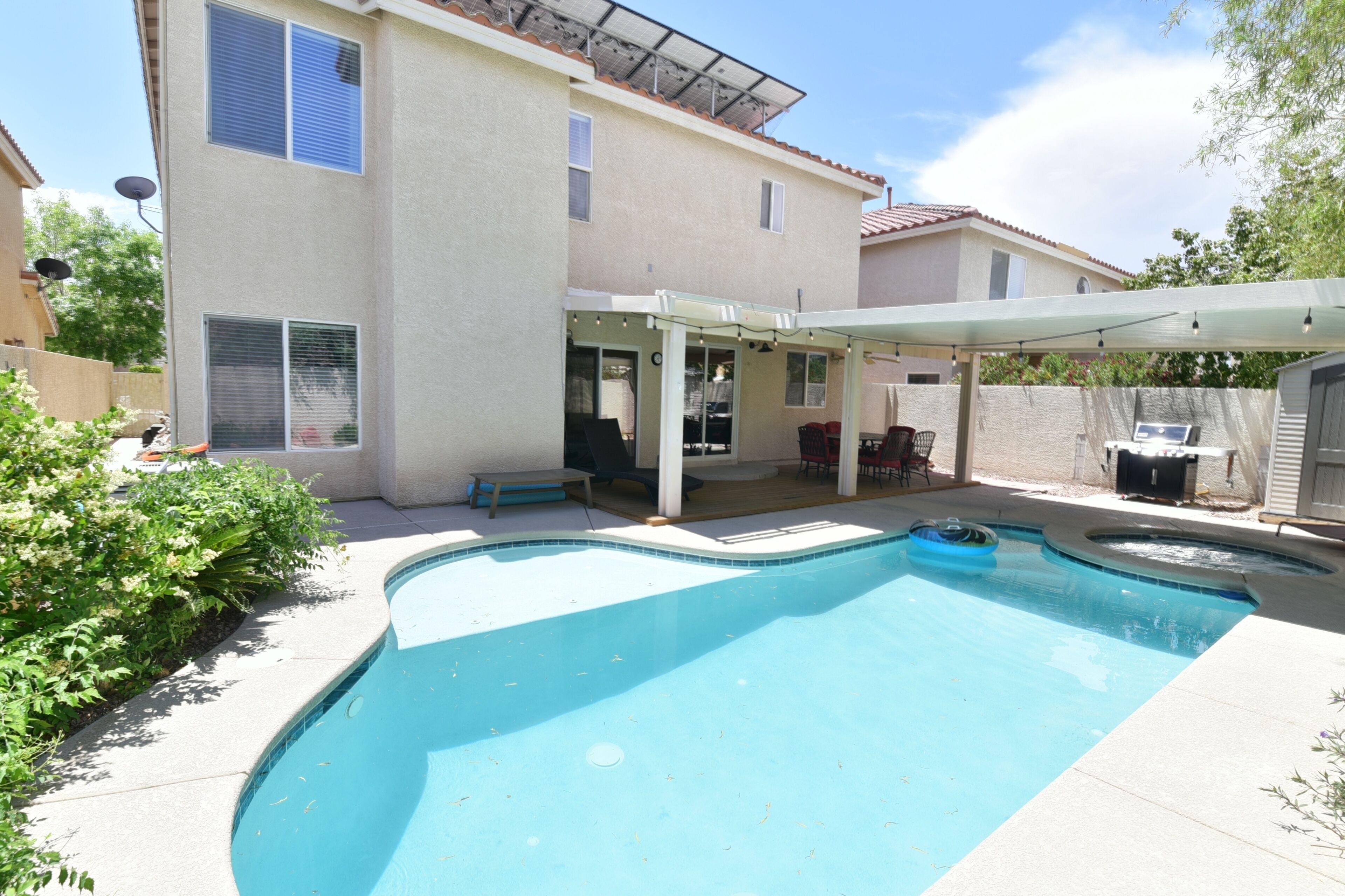 A backyard with a swimming pool, a covered patio, and a house.