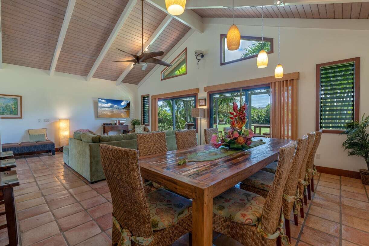 A spacious living area with a wooden dining table, wicker chairs, a sofa, and a ceiling fan.