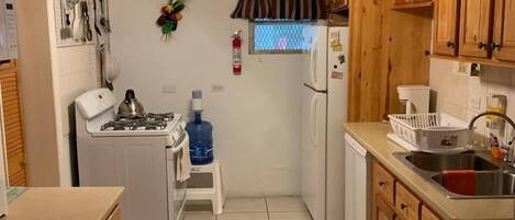 A compact kitchen with wooden cabinets, a gas stove, a refrigerator, and a ceiling fan.