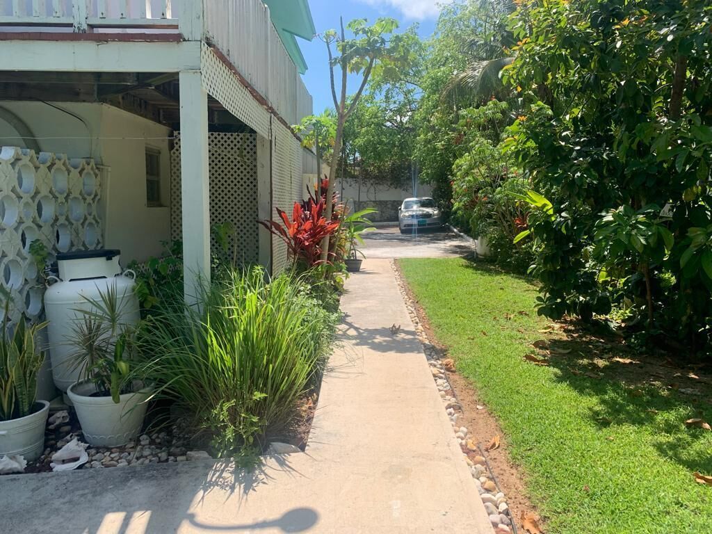 Un sendero conduce a una casa con porche cubierto, rodeada de macetas y follaje.