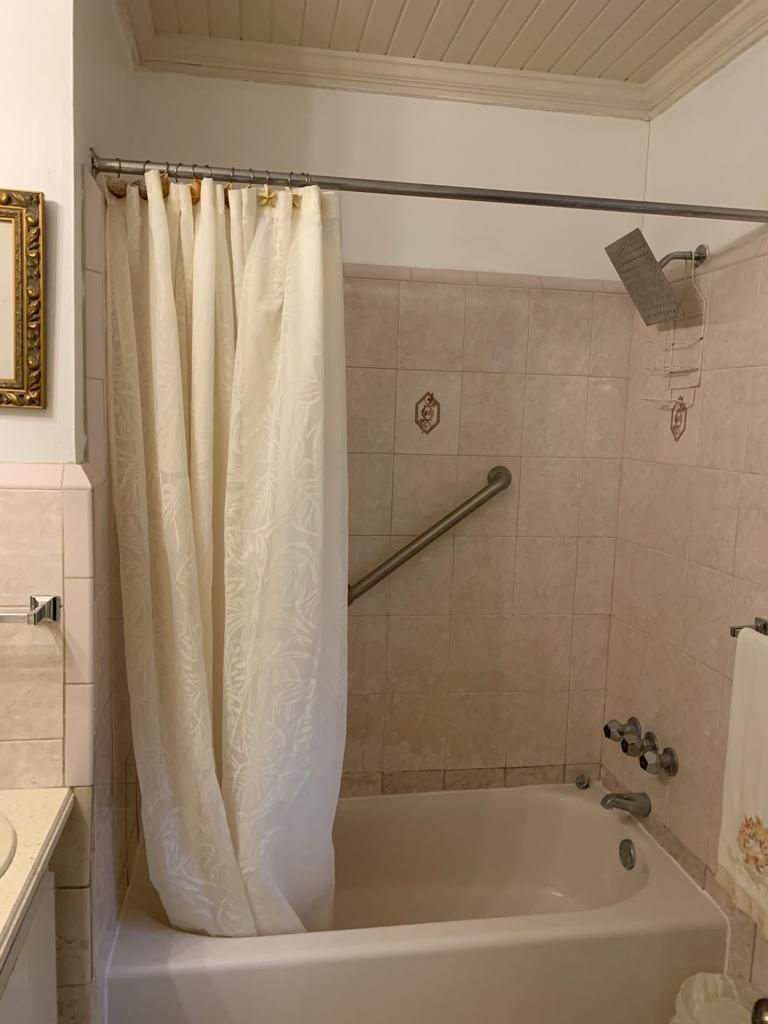 A bathroom with a bathtub, a shower with a grab bar, a towel rack, and a mirror with a decorative frame.