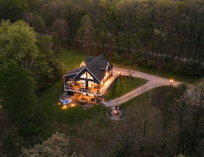 Une grande maison dotĂ©e dâun porche, dâun foyer extĂ©rieur et dâun espace extĂ©rieur bien Ă©clairĂ©.